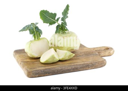 Ganze und geschnittene Kohlrabiknollen mit grünen Blättern, die auf einer strukturierten Holzplatte vor weißem Hintergrund angeordnet sind Stockfoto