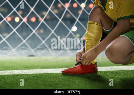 Nahaufnahme eines Fußballers in gelb-grüner Uniform, der einen roten Fußballschuh auf einem Stadionrasen bindet Stockfoto