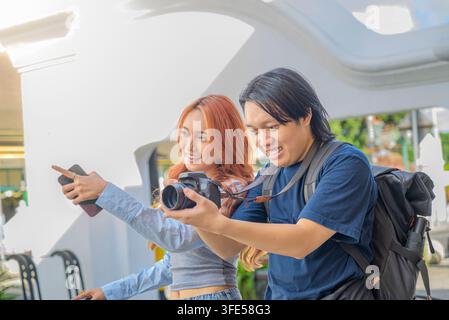 Ein glückliches junges indonesisches südostasiatisches Paar genießt das Reisen, macht Fotos mit einer DSLR-Kamera und einem Smartphone, während es gemeinsam Stadtansichten erkundet Stockfoto