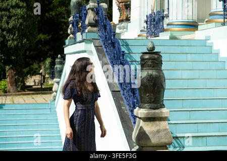 Elegante Touristin in blauem Kleid, die ein schönes historisches Gebäude und eine dekorative Treppe bewundert. Stockfoto