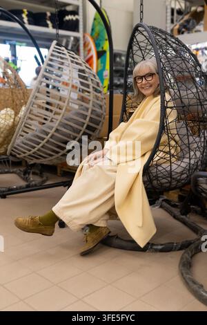 Zufriedene Seniorin sitzt in einem Eierstuhl während eines angenehmen Einkaufserlebnisses Stockfoto