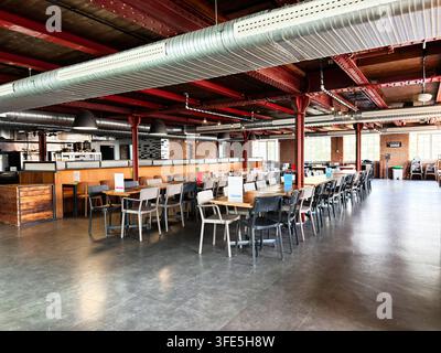 Manchester, UK - 02. Juli 2026: Geräumiger gemeinschaftlicher Speisesaal mit langen Holztischen, Metallstühlen und industrieller Decke in Manchester, UK Stockfoto