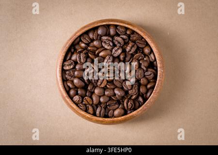Oberansicht von gerösteten Kaffeebohnen in einer Holzschale auf Kraftpapier-Hintergrund Stockfoto
