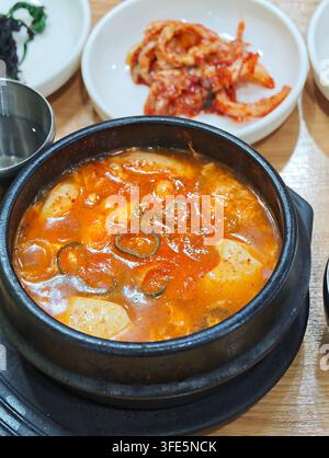 Traditionelles koreanisches Sundubu Jjigae, heiß serviert mit Kimchi-Beilage auf einem Holztisch in Korea. Stockfoto