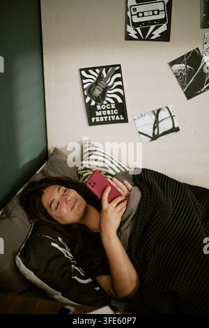 Bikolor Frau entspannt sich im Bett und surft auf dem Smartphone Stockfoto