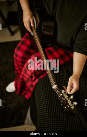 Frau stimmt akustische Gitarre während der Musikübung zu Hause Stockfoto