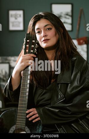 Porträt einer Musikerin, die drinnen eine Akustikgitarre hält Stockfoto