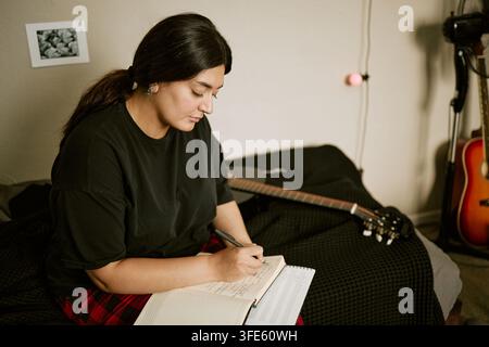 Bikolorische Frau schreibt Songtexte in ein Notizbuch zu Hause Stockfoto