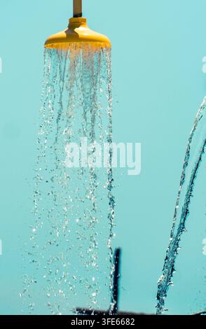 Gelber Außenduschkopf mit fallenden Wasserströmen vor einem türkisblauen Hintergrund. Stockfoto