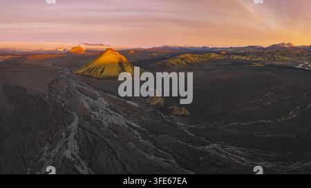 Luftbild des Vulkans Maelifell mit seinen lebendigen grünen moosigen Hängen, die aus den dunklen vulkanischen Sandebenen und den gewundenen Flussbetten unter einem Goldhimmel aufragen Stockfoto