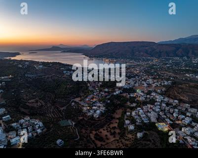 Luftaufnahme der Küstenstadt bei Sonnenuntergang mit Hafenlichtern, die gegen die dunkler werdenden Hügel und das Ägäische Meer in Chania, Griechenland, leuchten Stockfoto