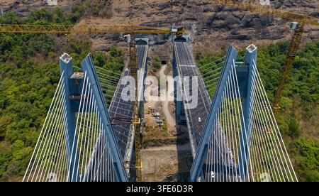 Luftbild der im Bau befindlichen Missing Link Hängebrücke mit Betonpfeilern, Stahlkabeln, Autobahnspuren, Tunneln und Kränen in L Stockfoto