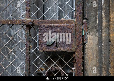 Eine detaillierte Nahaufnahme, die die starke Rosttextur auf einem alten Eisenschlosskasten mit einem Schlüsselloch und Drahtgittersieb zeigt. Stockfoto