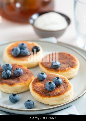 Leckere hausgemachte Quarkpfannkuchen serviert mit Blaubeeren auf einem Teller. Gesundes Morgenfrühstück mit Sauerrahm, süße Rezeptidee. Heller sauberer Hintergrund mit Kopierraum für Bannerdesign Stockfoto