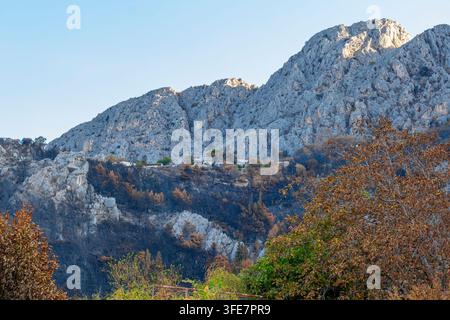 Die Rocky Mountains erheben sich über einem kleinen Hügeldorf in Kroatien bei klarem Tageslicht. Stockfoto