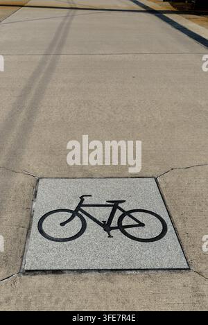 Fahrradsymbol in Stein auf einem Asphaltweg eingraviert, der als Fahrradweg dient und die richtige Spur für Fahrradfahrer anzeigt, um neben Fußgängern zu fahren Stockfoto