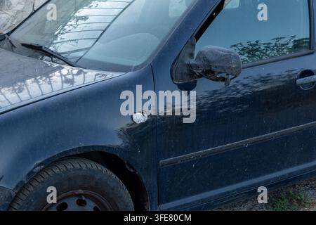 Ein schmutziges dunkelblaues Auto mit einem beschädigten Seitenspiegel wird im Nahaufnahme gezeigt. Stockfoto