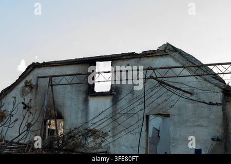 Ein beschädigtes verlassenes Haus steht unter einem blassen Himmel mit eingestürzten Dachteilen, freiliegenden Wänden und verworrenen Überkopfkabeln. Stockfoto