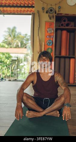 Latino-Mann lächelt in einem Yogastudio, sitzt in einer meditativen Pose Stockfoto