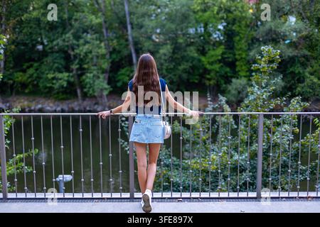 Junge Frau steht an einem Flusergeländer im Green Park. Junge Frau mit langen braunen Haaren steht in einem blauen Oberteil und gestreiftem Stockfoto