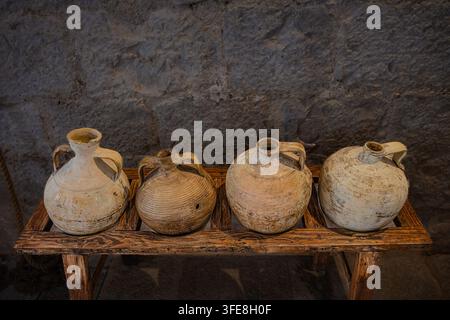 Vier antike keramische Wasseramphoren, die auf einem rustikalen Holzständer gegen eine Steinmauer im Castillo de Peñíscola platziert sind. Stockfoto