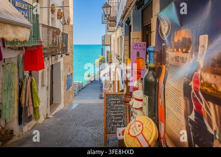 Eingang eines Souvenirladens in einer abschüssigen Gasse mit Blick auf das türkisfarbene Mittelmeer in Peñíscola, Spanien. Stockfoto