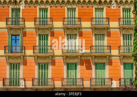 Symmetrische orangefarbene Gebäudefassade mit Reihen grüner Holzfensterläden und kunstvollen schmiedeeisernen Balkonen. Stockfoto
