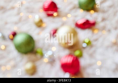 Verschwommene farbenfrohe Weihnachtskugeln, die über einen weichen, flauschigen weißen Teppich verstreut sind und einen festlichen Hintergrund bilden. Träumende leuchtende Heiligenscheine, ätherische Reflexionen Stockfoto