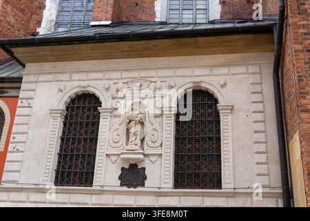 Krakau, Polen - 29.08.2026 Dekorative Kirchenwand zeigt eine geformte Heiligennische, gewölbte Buntglasfenster und detaillierte Steinverzierungen. Backsteinstruktur Stockfoto