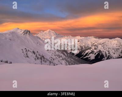 Atemberaubende winterliche Berglandschaft des Mount Baker bei Sonnenaufgang mit feurigen orangefarbenen Wolken über schneebedeckten Alpenkämmen. Stockfoto
