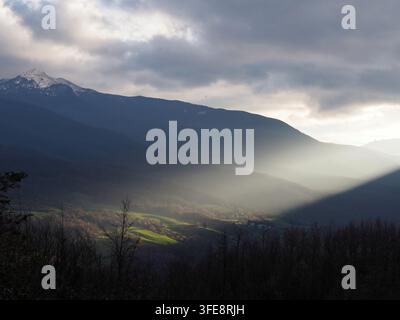 Sonnenstrahl trifft grüne Hügel durch Morgennebel in der Nähe von Rigoso. Stockfoto