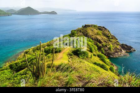 Hochwinkelaufnahme von üppigen grünen Hügeln, historischen Ruinen von Fort Rodney und türkisblauem Meer auf Pigeon Island in Saint Lucia. Stockfoto