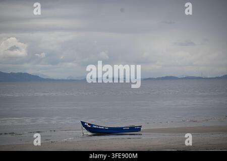 Ein kleines Tourboot ruht auf dem sandigen Ufer während der Ebbe in Punta Chame, Panama. Unter dramatischen Regenzeitwolken über dem Pazifik Stockfoto