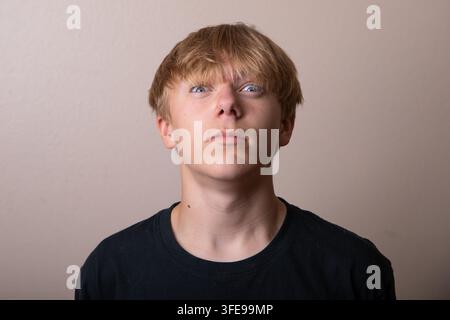 Ein junger Mann mit kahlgeschorenem Kopf und einem schwarzen Hemd schaut in die Kamera Stockfoto