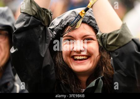 FRÖHLICHE FRAU FEIERT IM REGEN, REPORTAGE, GREEN MAN FESTIVAL 2019, BRECON, WALES, UK, 2019: Eine fröhliche junge Frau mit dunklen Haaren, die eine schwarze Kapuzenjacke trägt, lächelt breit mit erhobenen Armen während eines Regenschauers. Foto: Rob Watkins. INFO: Das Green Man Festival begann 2003 in Wales. Es findet jährlich an dem dritten Wochenende im August in den Brecon Beacons statt und feiert alternative Musik, Kunst, Literatur, Wissenschaft und familienfreundliche Kultur in einer wunderschönen Berglandschaft. Stockfoto
