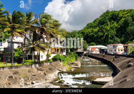 Ein wunderschöner Blick auf den Grand Riviere-Fluss mit kleinen Wasserfällen, die durch die tropische Stadt Grand Riviere in Martinique fließen, umgeben von Palmen und üppigen Hügeln Stockfoto
