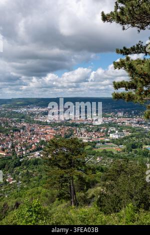 Weitläufige Luftaufnahme von Jena, Thüringen, mit roten Dächern, Stadtsilhouette und sanften Hügeln unter einem dramatischen bewölkten Himmel. Stockfoto