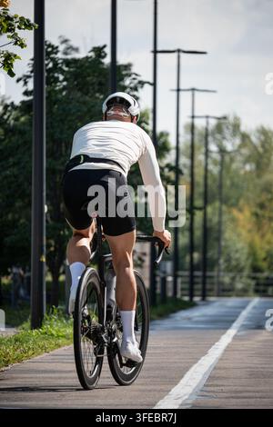 Rückansicht eines athletischen männlichen Radfahrers, der ein Rennrad auf einem ausgewiesenen Radweg im Freien fährt. Radfahren-Training, Ausdauer und aktives Verkehrsmittel-Konzept. Stockfoto