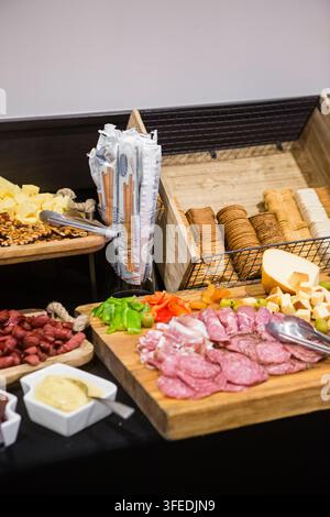 Ein reichhaltiger Schinkbuffet-Tisch mit aufgeschnittenen Schinkensorten, verschiedenen Käsesorten, Crackern, Baguettestangen, Paprika und Beilagen auf einem Holzserviertablett Stockfoto