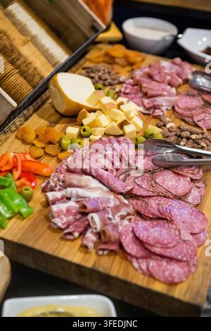 Schneidebrett mit gepökelten Fleisch, geschnittenem Salami, Käsewürfeln, Oliven, Nüssen, getrockneten Früchten und Crackern, serviert auf einer Holzplatte für eine Party Stockfoto
