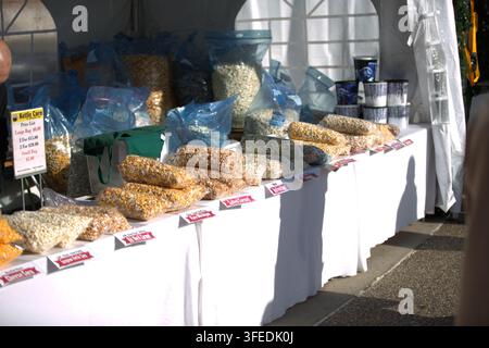 Ein Marktstand, der verschiedene verpackte Geschmacksrichtungen von Gourmet-Kettle Corn und Popcorn auf einem langen weißen Tisch anbietet. Stockfoto