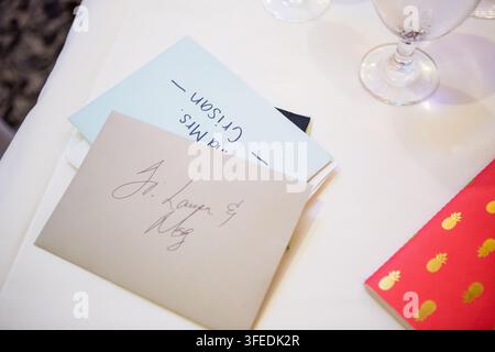 Handgeschriebene Gästesiegel und Platzkarten, die auf einem weißen Tischtuch an einem Hochzeitsempfangstisch platziert sind. Stockfoto