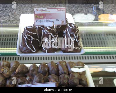 Schokoladenüberzogene birnenförmige Gebäckstücke mit weißer Zuckerglasur, die auf einem Tablett in einer Bäckereivitrine ausgestellt sind. Stockfoto