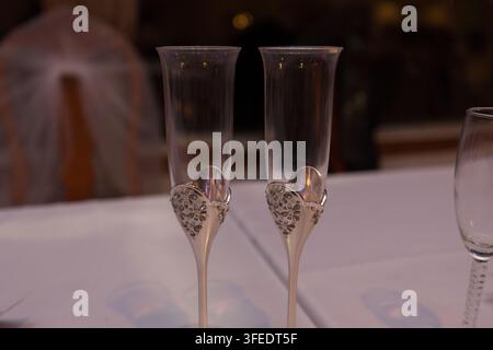 Ein Paar elegante Champagnerflöten, verziert mit kunstvollem Silber und Kristallen auf einer weißen Tischdecke bei einer Hochzeitsfeier. Stockfoto