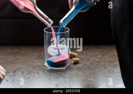 Rosa und blau gefärbter Sand wird gleichzeitig aus zwei Glasflaschen in einen zentralen Glasbehälter gegossen während einer Vereinigungssandzeremonie. Stockfoto