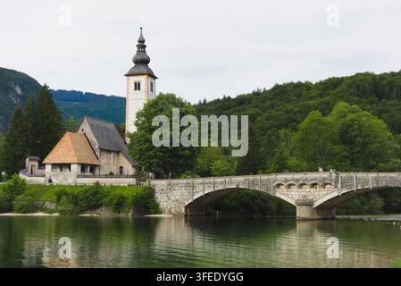 Historische Steinbrücke und Kirche St. Johannes der Täufer spiegeln sich im Bohinj-See in Ribčev Laz, Triglav-Nationalpark, Slowenien. Stockfoto