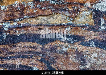 Verwitterte Sandstein-Felsenstruktur mit bunten Mineralbändern und Flechtengrowth Stockfoto