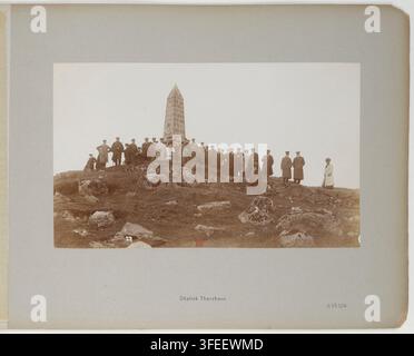 Eine Gruppe von Menschen, meist in dunklen Mänteln und Hüten gekleidet, stehen und sitzen um ein hohes, spitzes Steinmonument, den Obelisk Thorshavn, auf einem felsigen Hügel, bei Atelier Schaul im Jahr 1907, während einer Reise zu den Nordländern und Inseln, einschließlich Schottland, den Färöer-Inseln und Island, an Bord des Hamburg-Amerika-Linie-Schiffs "Oceana". Stockfoto