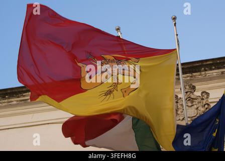 Flagge Siziliens mit dem Trinacria-Symbol, das vor einem klaren blauen Himmel in Italien weht. Stockfoto