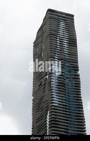 Vertikalfoto eines modernen Glasgebäudes mit einer markanten wellenförmigen Fassade, das fließende architektonische Linien und reflektierende Oberflächen präsentiert Stockfoto